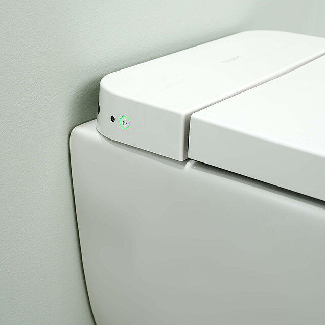 Nahaufnahme einer modernen weißen, intelligenten Toilette mit geschlossenem Deckel und einem grün leuchtenden Einschaltknopf 