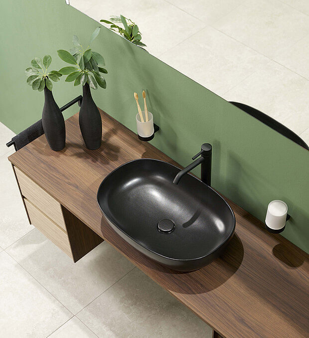 Badezimmer-Arbeitsplatte mit einem schwarzen ovalen Waschbecken, einem schwarzen Wasserhahn, zwei schwarzen Vasen.