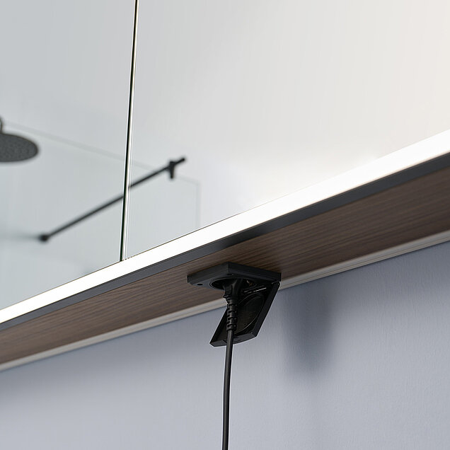 Nahaufnahme einer Steckdose unter einem an der Wand befestigten Badezimmer-Spiegelschrank 