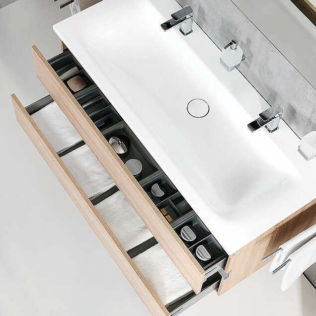 Sicht von oben auf einen Waschtisch mit weißem Becken und zwei offenen Holzschubladen.