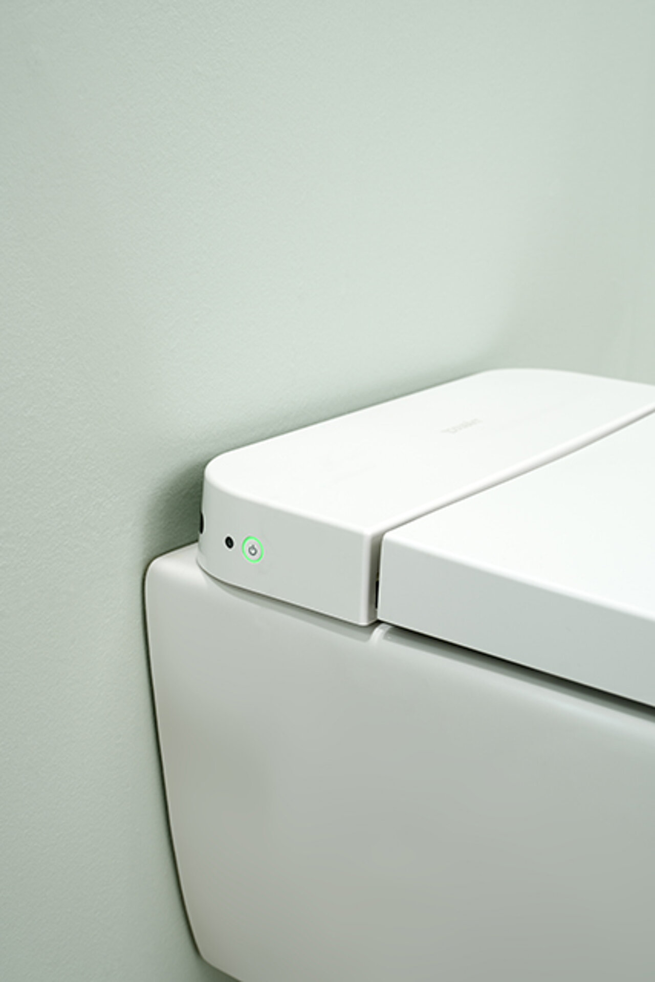Eine Nahaufnahme einer modernen weißen Toilette mit schlichtem, minimalistischem Design und einem Kontrollknopf mit grünem Licht 