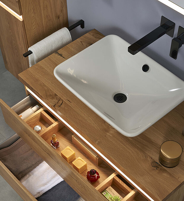 Badezimmer-Waschtisch mit weißem, rechteckigem Waschbecken, schwarzem Wasserhahn, hölzerner Arbeitsplatte und offener Schublade.