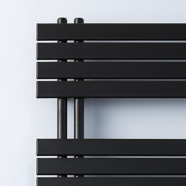 Nahaufnahme eines modernen, schwarzen Badheizkörpers vor einer schlichten, hellen Wand. 