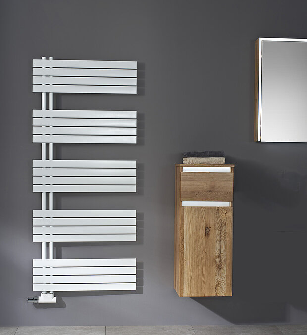 Ein Badezimmer mit einer dunkelgrauen Wand, einem weißen Badheizkörper und einem hölzernen Wandschrank daneben.