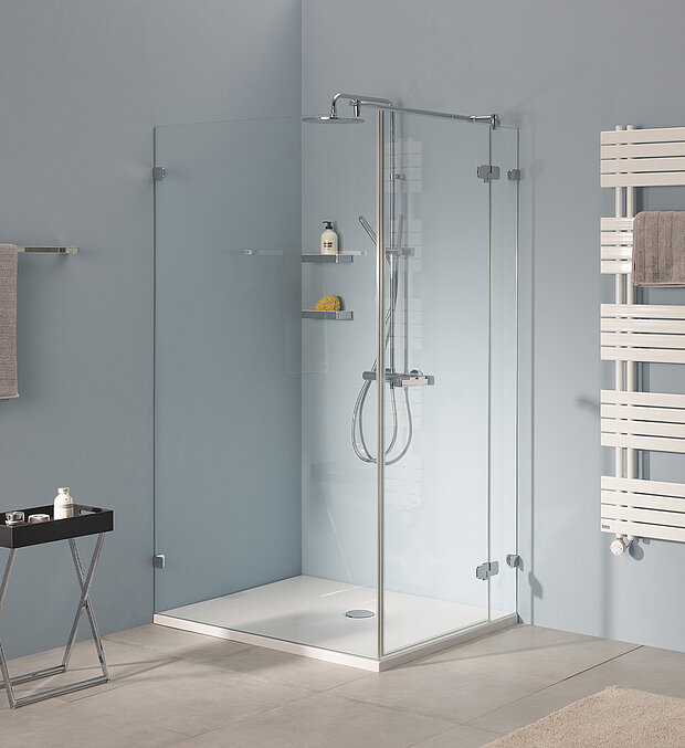 Ein modernes Badezimmer mit verglaster Eckdusche und Handbrause, Ablagen für Toilettenartikel sowie weißem Badheizkörper.