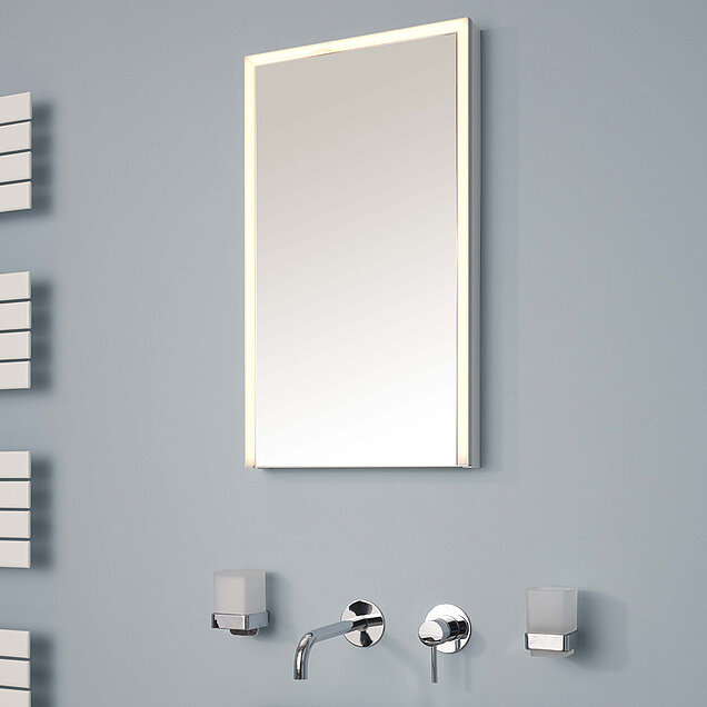   Ein rechteckiger Badezimmerspiegel mit eingebauter LED-Beleuchtung hängt an einer grauen Wand.
