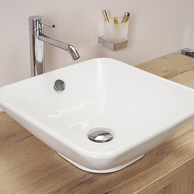 Ein modernes weißes, quadratisches Keramikwaschbecken mit einem verchromten Wasserhahn.