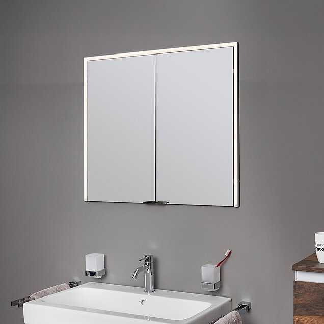 Ein viereckiger, silbergerahmter Wandeinbauspiegelschrank mit LED-Licht auf drei Seiten.