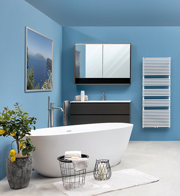Badezimmer mit blauen Wänden, einer weißen freistehenden Badewanne, einem Wandwaschbecken mit Spiegel, einem Handtuchwärmer.