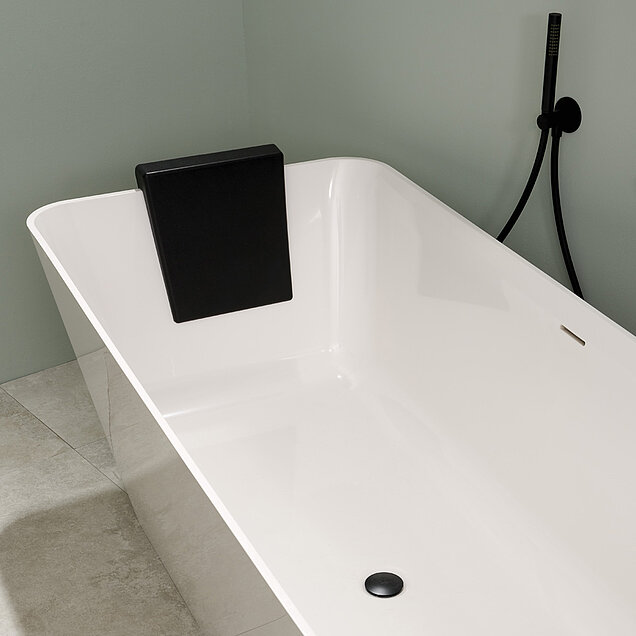 Eine moderne weiße Badewanne mit schwarzer Kopfstütze, schwarzer Ablaufabdeckung und schwarzer Handbrause.
