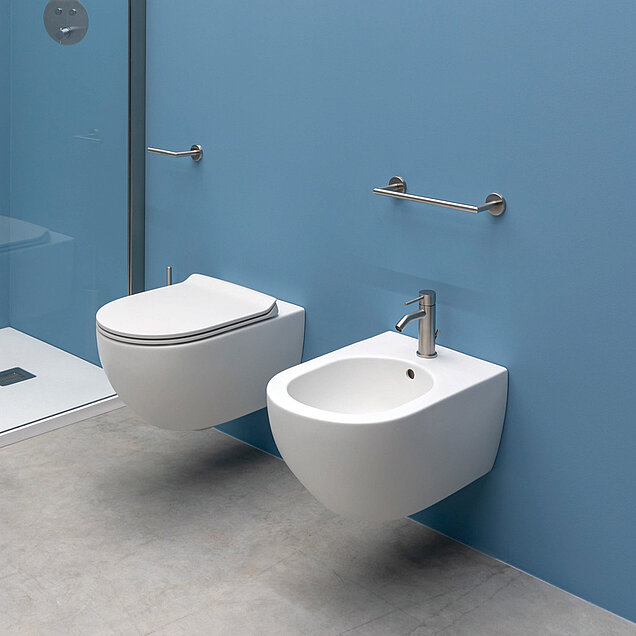 Wandmontierten Toilette und einem Bidet, beide weiß, vor einer blauen Wand.