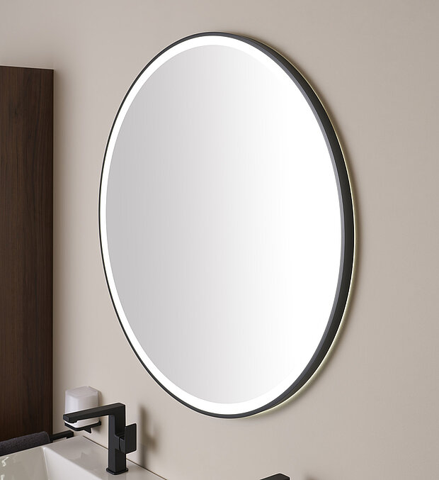 Ein runder, an der Wand montierter Spiegel mit beleuchtetem Rand befindet sich über einem modernen Waschbecken.