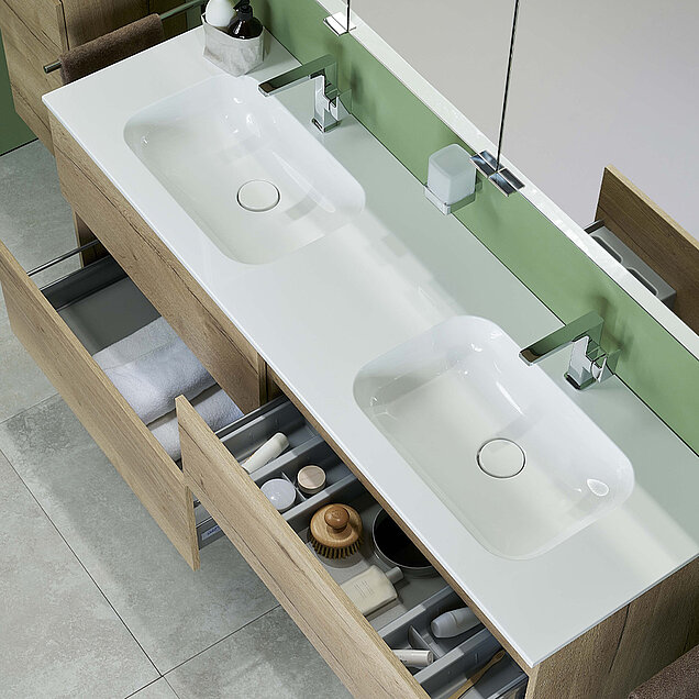 Waschtisch mit zwei rechteckigen Waschbecken und mehreren offenen Holzschubladen, in denen sich Handtücher und verschiedene Toilettenartikel befinden.