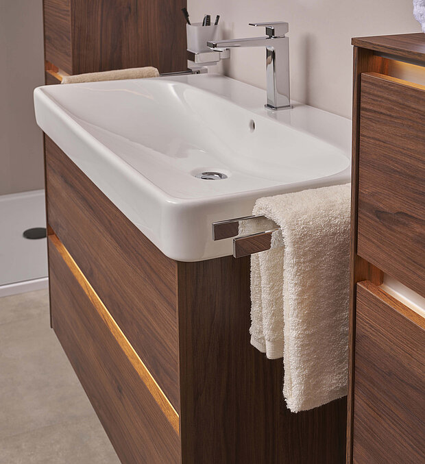 Rechteckiges weißes Badezimmerwaschbecken mit verchromtem Wasserhahn und dunklem Holzwaschtisch. 