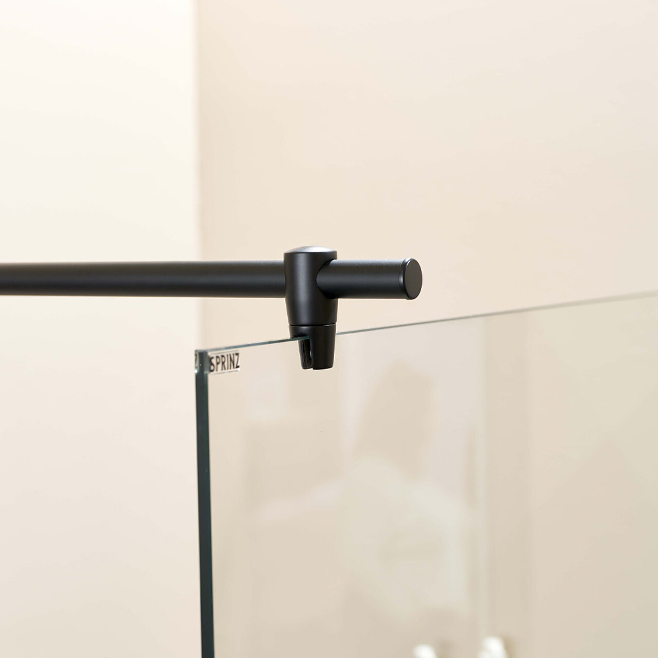 Nahaufnahme einer schwarzen Metallstange, die am oberen Rand einer Glasduschwand befestigt ist