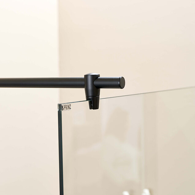 Nahaufnahme einer schwarzen Metallstange, die am oberen Rand einer Glasduschwand befestigt ist