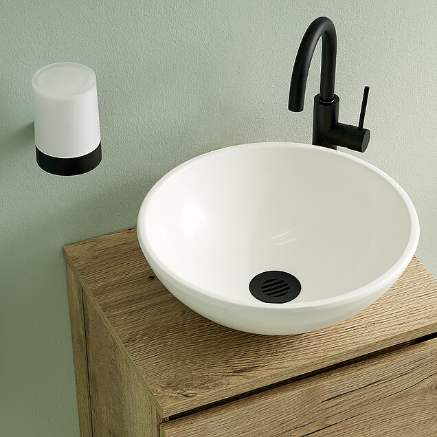 Ein modernes Waschbecken mit einem runden weißen Becken auf einem hölzernen Waschtisch, einem schwarzen Wasserhahn