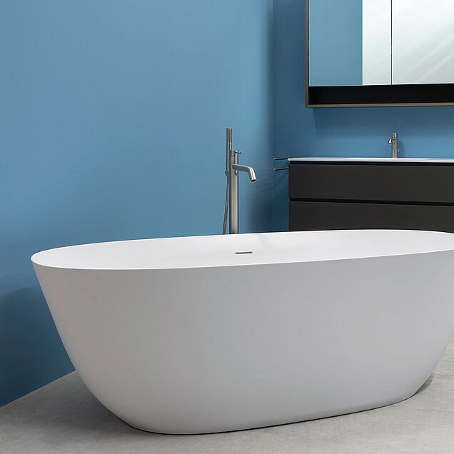 Badezimmer mit einer weißen, freistehenden Badewanne, einem hellgrauen Boden, blauen Wänden, einem eleganten silbernen Wasserhahn.