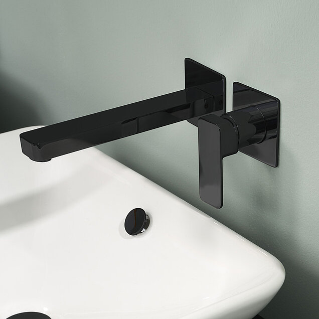 Mattschwarze Wandarmatur und Griff über einem weißen rechteckigen Waschbecken mit passender schwarzer Ablaufabdeckung 