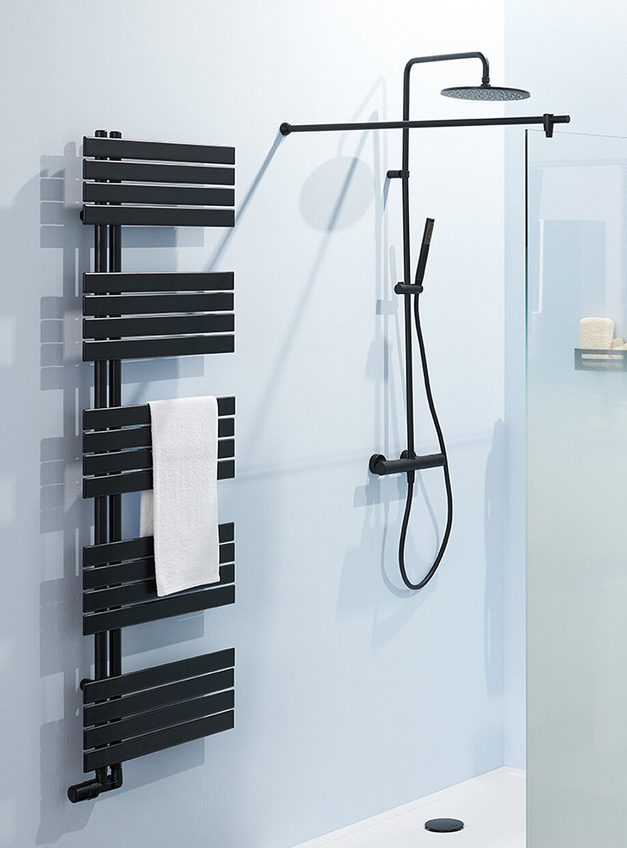 Modernes Bade mit einer begehbaren Dusche mit schwarzem Regenbrausekopf, Trennwand aus Milchglas, schwarzem Handtuchheizkörper mit weißem Handtuch.