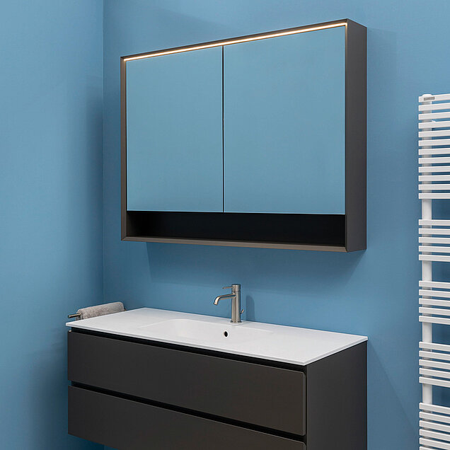 Badezimmer mit hellblauen Wänden, einem schlichten dunklen Waschtisch mit weißem Waschbecken und einem Spielgeschrank.