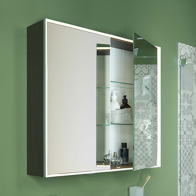 Badezimmerschrank mit Spiegeltüren, von denen eine leicht geöffnet ist, um Regale mit Toilettenartikeln zu zeigen.