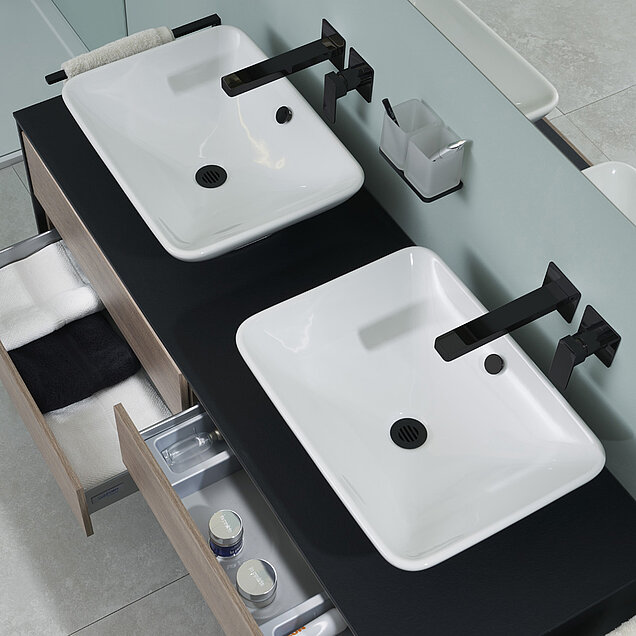 Badezimmer-Waschtisch mit zwei rechteckigen weißen Waschbecken, schwarzen Armaturen, offenen Schubladen.