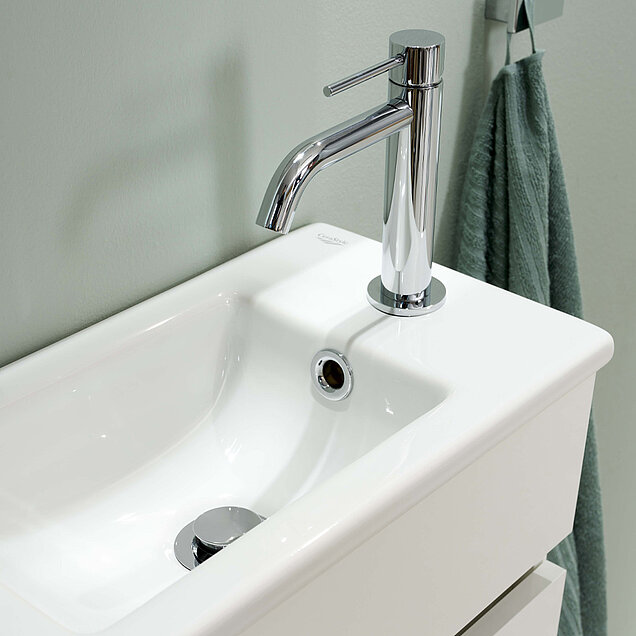 Weißes Waschbecken mit einem chromglänzenden Wasserhahn.