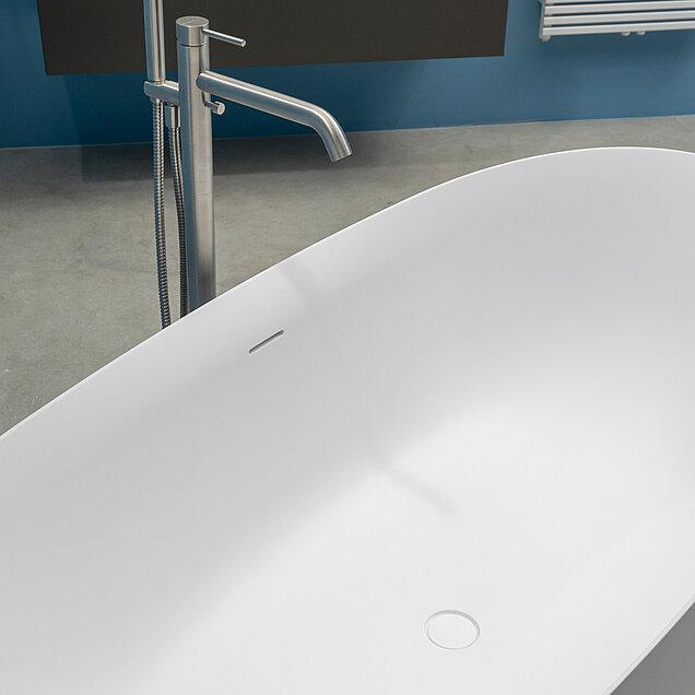 Eine moderne, weiße, freistehende Badewanne mit einer eleganten, silbernen Bodenarmatur.