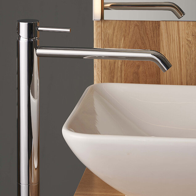 Nahaufnahme eines modernen verchromten Wasserhahns neben einem weißen rechteckigen Waschbecken.