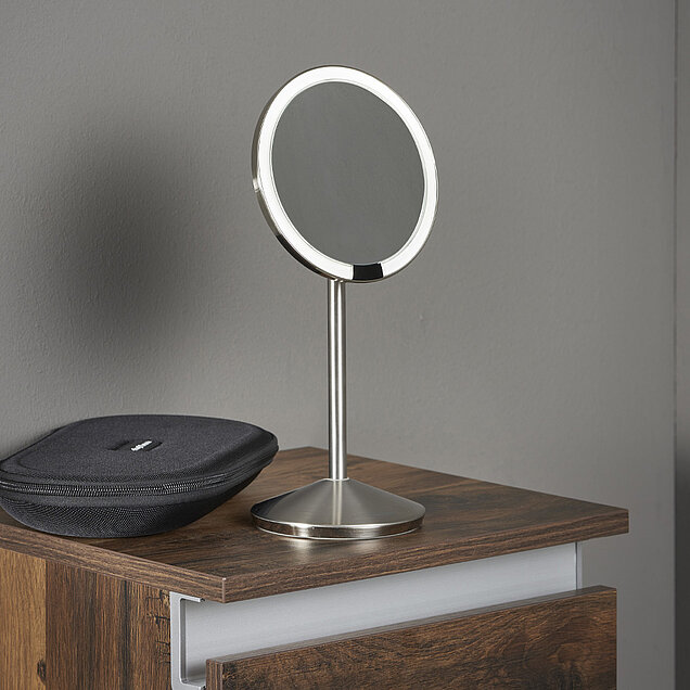 Ein runder, silbergerahmter Kosmetikspiegel steht auf einer hölzernen Kommode.