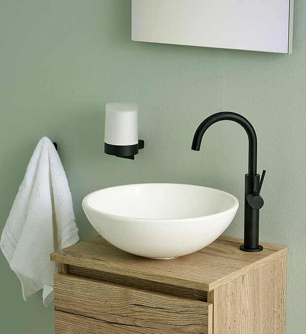 Rundes, weißes Waschbecken auf einem hölzernen Waschtisch mit einem schwarzen Wasserhahn.