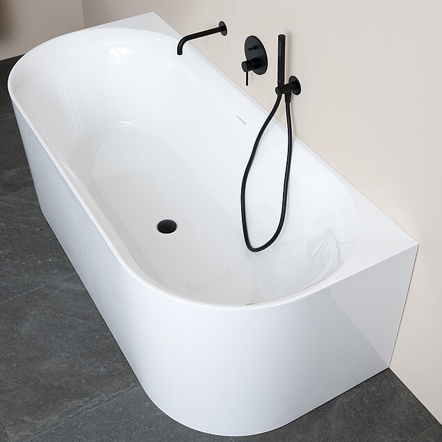 Eine moderne weiße Badewanne mit mattschwarzer Wandarmatur und Handbrause an einer Wand 