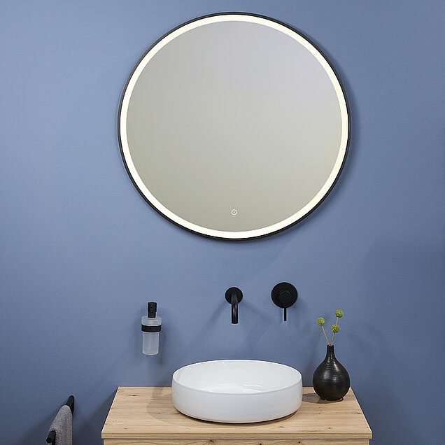 Ein modernes Badezimmer mit einem runden, hinterleuchteten Spiegel über einem hölzernen Waschtisch