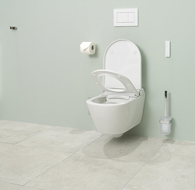 Ein modernes Dusch-WC mit offenem Deckel, einer Toilettenbürste, einem wandmontierten Toilettenpapierhalter mit Rolle und einer Spülplatte