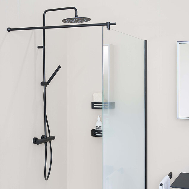 Eine moderne Dusche mit einer schwarzen Regendusche und einer Handbrause, die an einer beigen Wand neben einer Duschwand aus Milchglas montiert ist. 