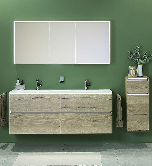 Badezimmer mit einem Doppelwaschbecken mit hellen Holzschränken, zwei Wasserhähnen, Spiegelschränken darüber und einem kleinen passenden Schrank daneben.