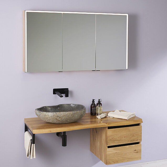 Ein moderner Waschtisch mit Arbeitsplatte aus Holz, einem Waschbecken aus Stein, einem schwarzen Wasserhahn und einem großen Spiegelschrank darüber