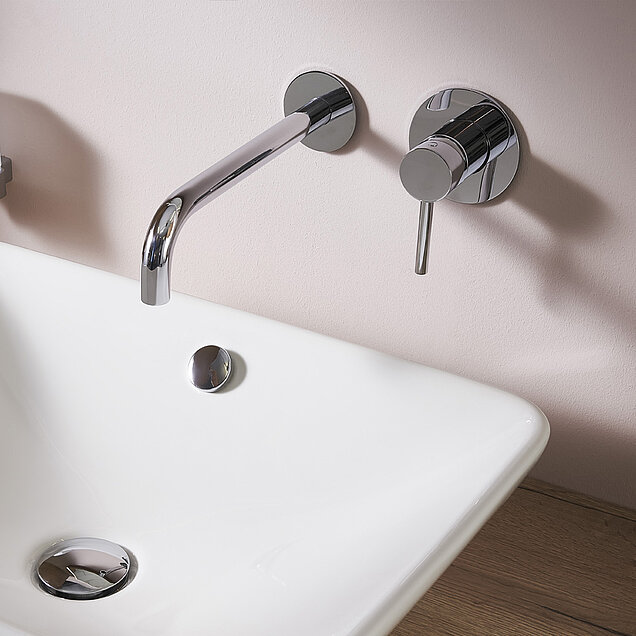 Moderne Chrom-Wandarmatur über einem weißen Waschbecken