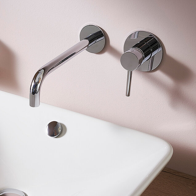 Besondere Armatur, zweigeteilt in chrome, Hebel für die Bedienung extra an der Wand und auch der Hahn ist extra an der rosafarbenen Wandmontiert