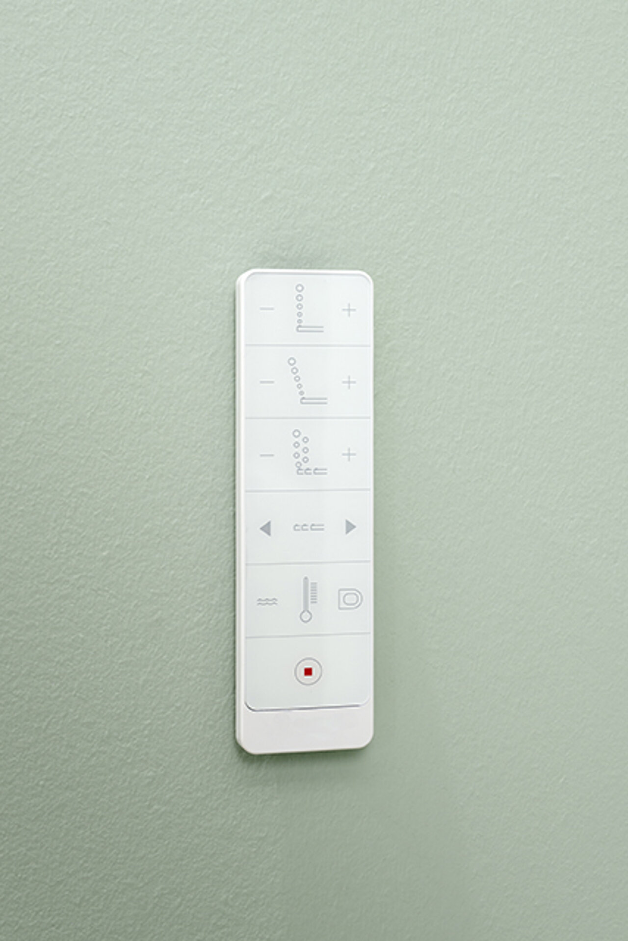 Fernbedienung mit minimalistischen Tasten ist an einer hellgrün strukturierten Wand angebracht