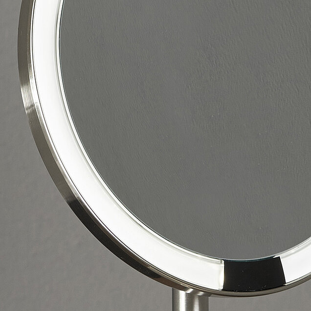 Nahaufnahme eines runden Tischspiegels mit silbernem Rahmen und eingebauter LED-Beleuchtung am Rand.