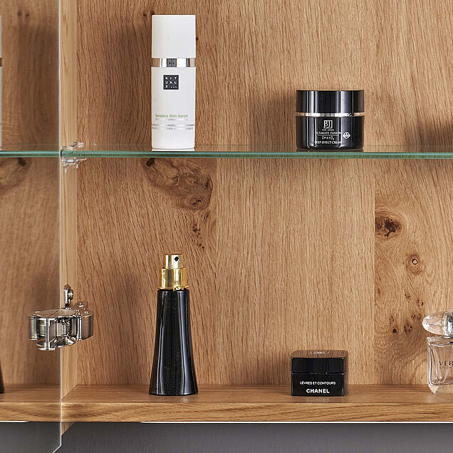 Eine Holzvitrine mit Glasböden enthält verschiedene Hautpflege- und Parfümprodukte.