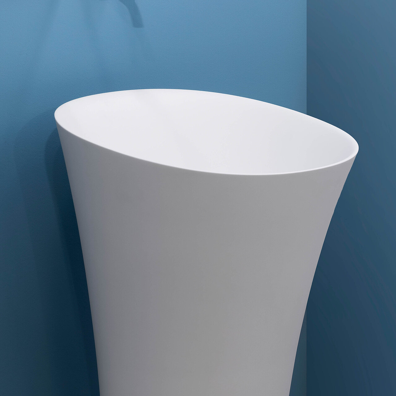 Eine blaue Wand im Hintergrund und ein freistehendes modernes Waschbecken der Produktlinie LARIMAR CAPRI