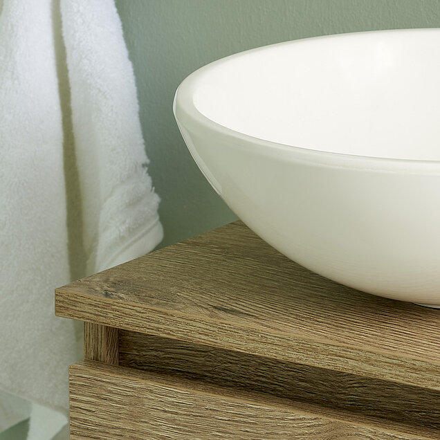 Weißes Keramikwaschbecken steht auf einem hellen Holzwaschtisch.