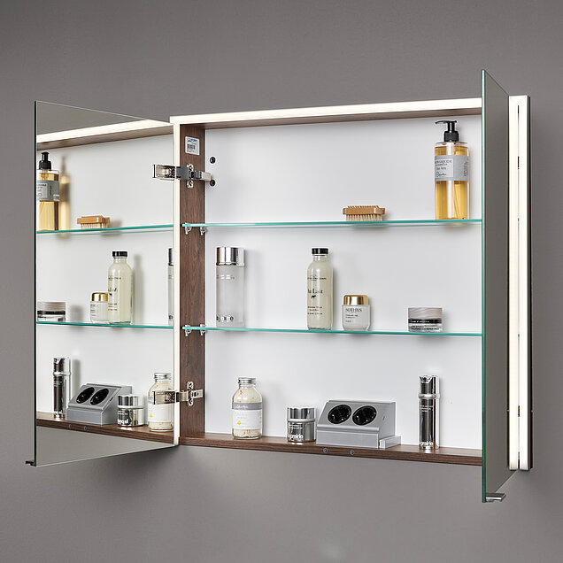 Ein Wandeinbauspiegelschrank der geöffnet ist und die Aufteilung innen zeigt mit einer Steckdosenleiste und zwei Einlegeböden.