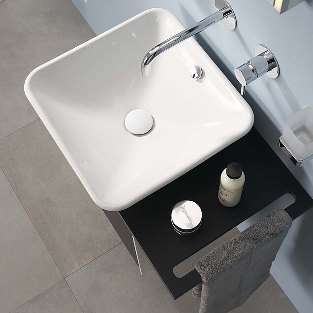 Quadratischen weißes Waschbecken auf einer schwarzen Arbeitsplatte und einem an der Wand montierten verchromten Wasserhahn.