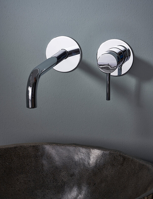 Eine moderne Chromarmatur über einem dunklen Waschbecken aus Stein.