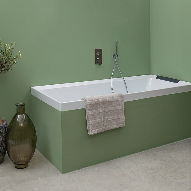 Badewanne vor einer grünen Wand mit einem verchromten Wasserhahn und einer Handbrause