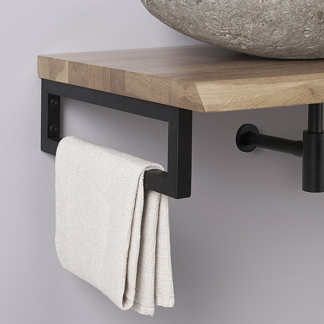 Ein gefaltetes weißes Handtuch hängt an einem schwarzen Handtuchhalter aus Metall, der unter einer hölzernen Arbeitsplatte mit einem steinernen Waschbecken darüber angebracht ist.